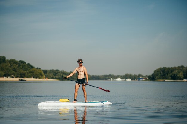 Un joven atlético rema parado en una tabla de sup en el río y mira hacia un lado