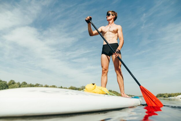 Joven atlético rema en una tabla de sup en el río Entrenamiento en una tabla de remo