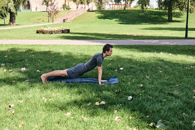 Joven atlético en ropa deportiva haciendo yoga en el parque. Practica asanas al aire libre. Personas que hacen ejercicio sobre la hierba verde con estera de yoga. Hombre caucásico maduro fuerte en pose de tablón de saludos dsun