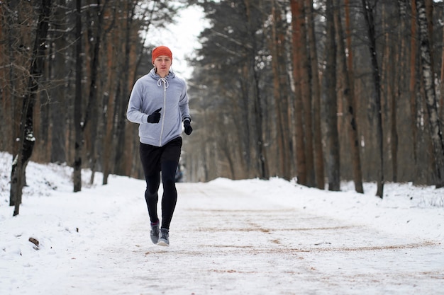 Joven atlético runing en bosque de invierno