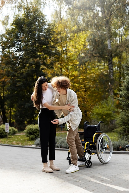 Una joven atractiva ayuda a un joven a levantarse de una silla de ruedas