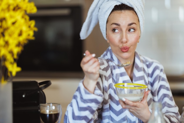 Una joven atractiva en bata de baño comiendo cereales para desayunar en casa.