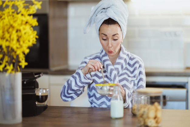 Una joven atractiva en bata de baño preparando un cereal para el desayuno en la cocina de casa.