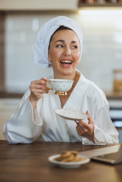 Una joven atractiva en bata de baño relajándose y bebiendo un café matutino en su casa.