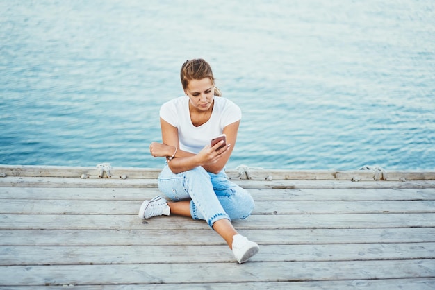 Joven atractiva chica hipster revisando la notificación en el teléfono inteligente con conexión 4g al aire libre