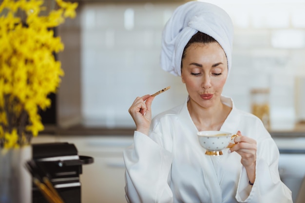 Una joven atractiva disfrutando de un café matutino y galletas en su cocina en casa.