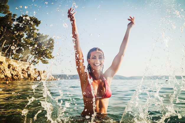 Una joven atractiva divirtiéndose y chapoteando en el agua del mar. Ella disfruta de vacaciones.