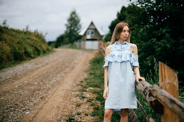 Foto joven atractiva elegante rubia en vestido azul romántico posando en la carretera en el campo