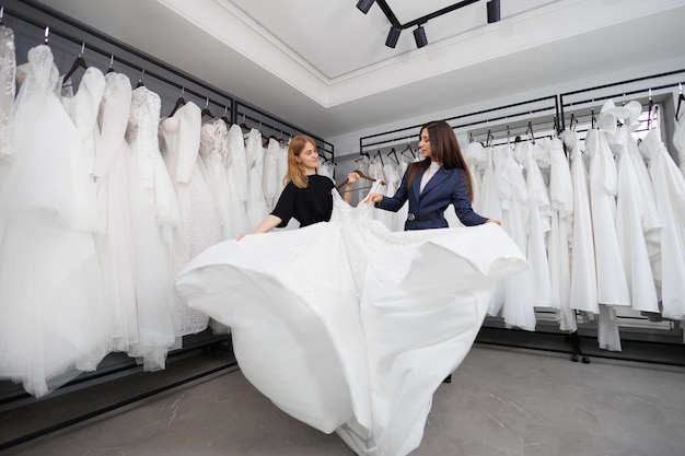 Una joven atractiva eligiendo un vestido blanco con la ayuda de un asistente de tienda en un salón de bodas.