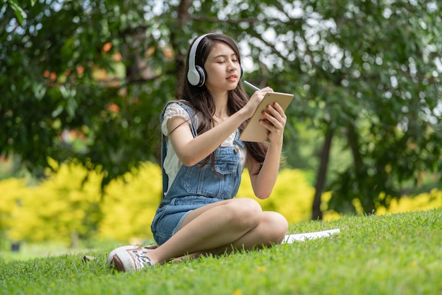 Joven y atractiva empleada asiática usa auriculares para escuchar el estudio de desarrollo de cursos digitales en línea en el parque