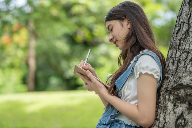 Joven y atractiva empleada asiática usa auriculares para escuchar el estudio de desarrollo de cursos digitales en línea en el parque