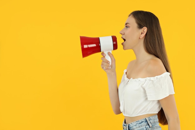 Una joven atractiva está de pie sobre un fondo amarillo con un altavoz