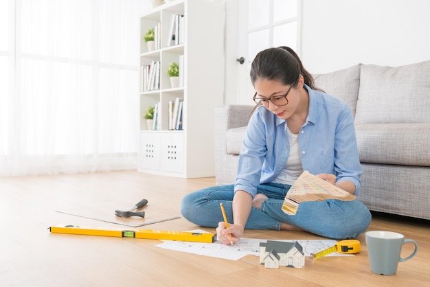 Foto joven y atractiva estudiante universitaria sentada en el suelo de madera de la sala de estar usando la herramienta de paleta eligiendo el color para el interior de la casa de diseño.