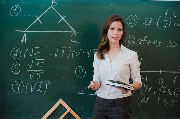 Foto joven y atractiva maestra de matemáticas que interactúa con sus jóvenes estudiantes de primaria que le piden una respuesta a una niña