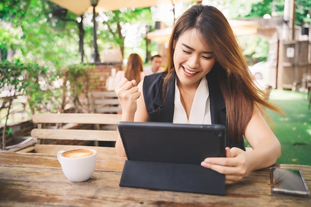 Joven atractiva mujer asiática independiente en sentirse feliz con un gesto sí está usando tableta y teléfono inteligente