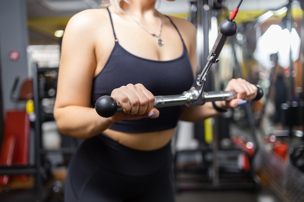 Una joven y atractiva mujer deportiva entrena tríceps en una máquina de ejercicios de cable cruzado en el gimnasio