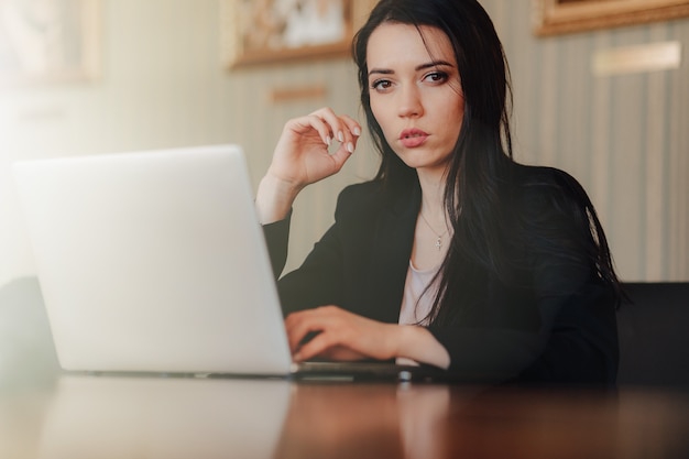 Joven atractiva mujer emocional en ropa de estilo empresarial sentado en el escritorio con una computadora portátil