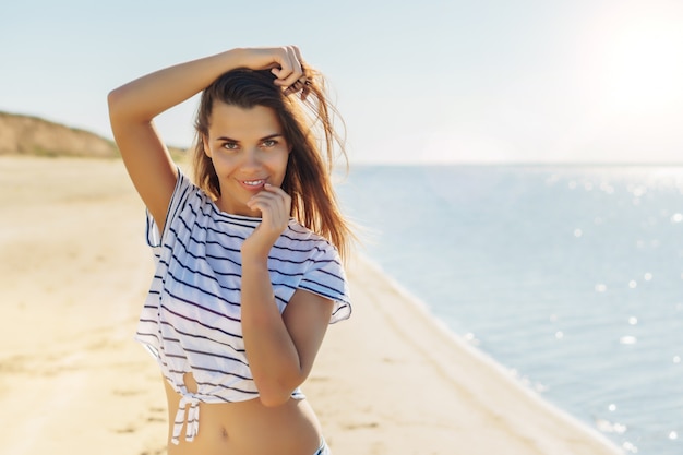 Joven atractiva mujer morena en camisa a rayas blancas disfrutando el verano con mar