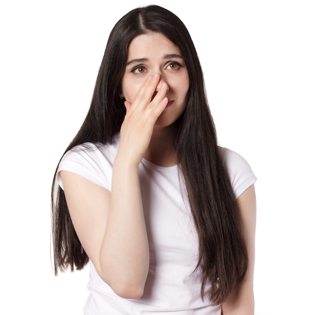 Joven y atractiva mujer morena de pelo negro caucásico en camiseta blanca, manos cerca de su rostro, idea de concepto de mujer molesta y llorando