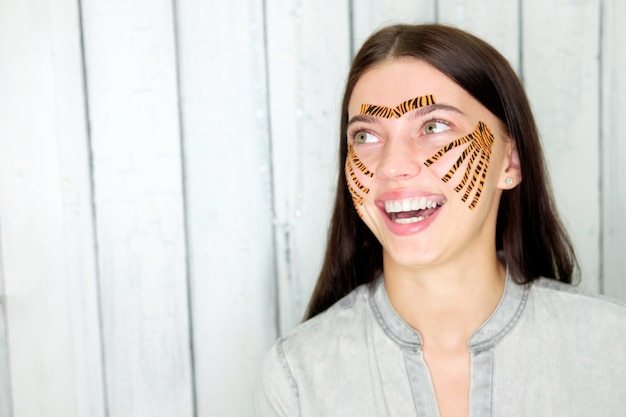 Joven y atractiva mujer morena sonriente con cintas de color tigre después de grabar el procedimiento facial en el salón de belleza