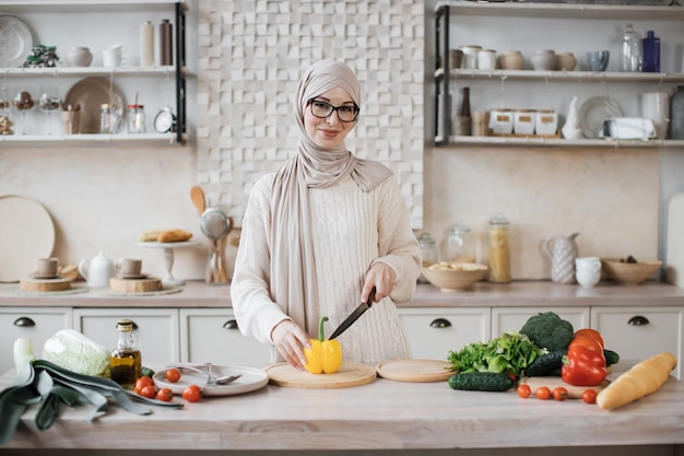 Joven atractiva mujer musulmana feliz en hijab preparando ensalada de verduras frescas
