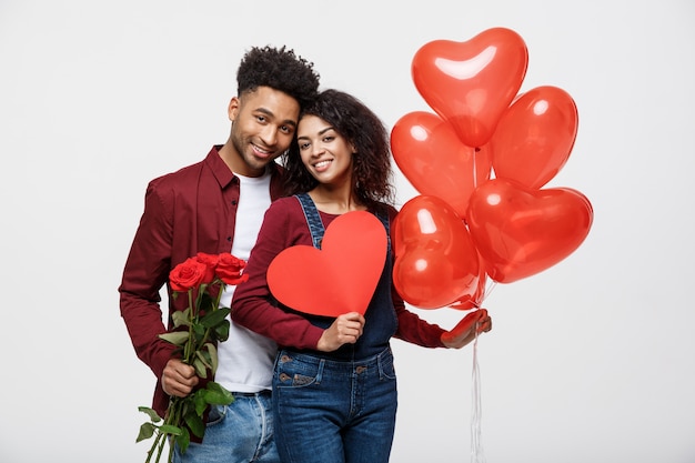 Foto joven atractiva pareja afroamericana en citas con rosa roja, corazón y globo.