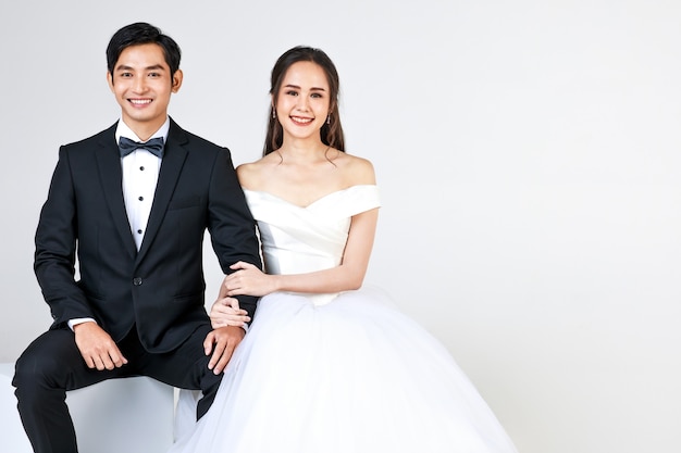 Joven atractiva pareja asiática, que pronto será la novia y el novio, mujer vestida con vestido de novia blanco. Hombre vestido con esmoquin negro, sentados juntos. Concepto de fotografía previa a la boda.