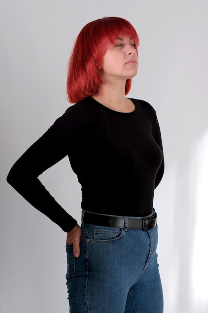 Una joven atractiva con un peinado corto de color naranja con una camiseta negra y jeans posando en el estudio sobre un fondo blanco.