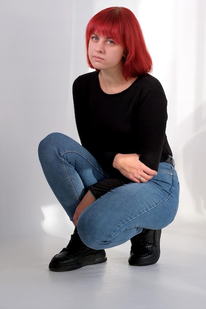 Una joven atractiva con un peinado corto de color naranja con una camiseta negra y jeans posando en el estudio sobre un fondo blanco.