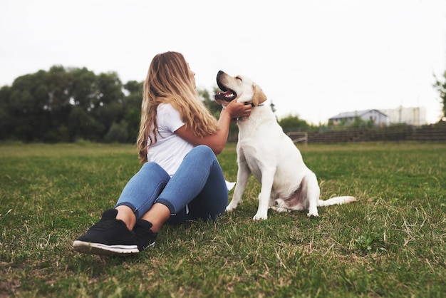 Joven atractiva con perro al aire libre. mujer en una hierba verde con labrador retriever