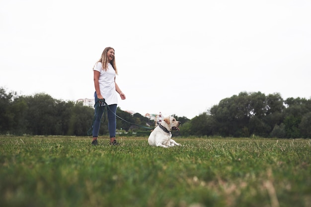 Joven atractiva con perro al aire libre. mujer en una hierba verde con labrador retriever