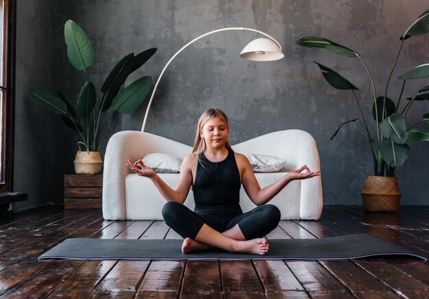 Una joven atractiva practicando yoga sentada en el ejercicio Half Lotus Ardha Padmasana plantean ejerciendo una sesión de meditación en el interior de su casa