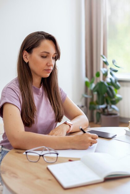 Foto una joven atractiva se sienta en una mesa y escribe en un bloc de notas