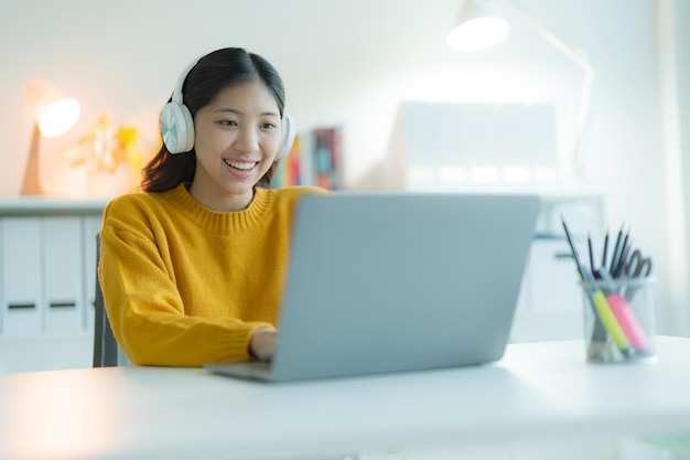 Una joven atractiva usa una computadora portátil en su oficina de casa con auriculares sonriendo