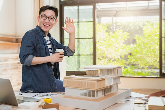 Joven atractivo asiático anteojos arquitecto masculino sonrisa seguro orgulloso de presentar nuevo proyecto casa modelo felicidad asiático trabajando con estudio de modelo masivo del proyecto de diseño de casa