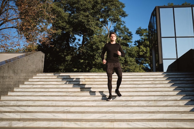 Joven, atractivo y confiado hombre deportivo corriendo por la mañana en el parque de la ciudad