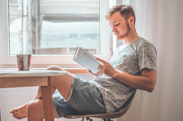 Joven atractivo está leyendo un libro en casa