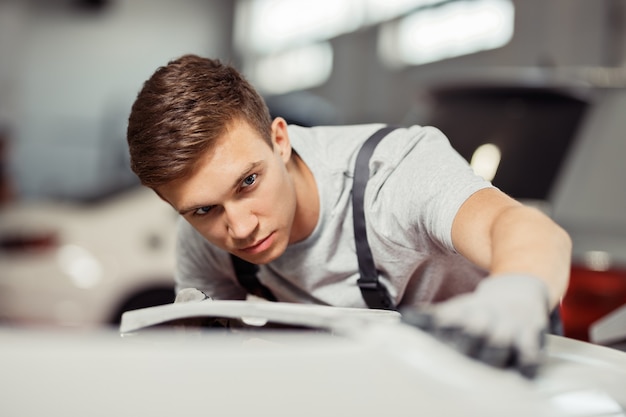 Un joven atractivo está puliendo un coche blanco.