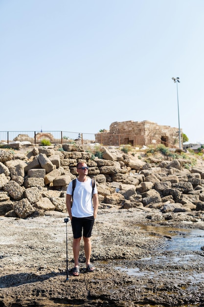 Joven atractivo con gafas de sol en una camiseta blanca y pantalones cortos se encuentra en la orilla del mar mediterráneo