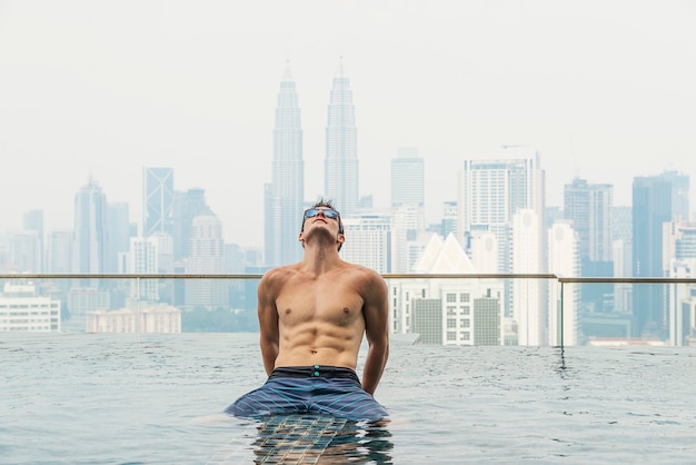 joven atractivo con gafas de sol en la piscina en la azotea del rascacielos. Está en kuala lumpur