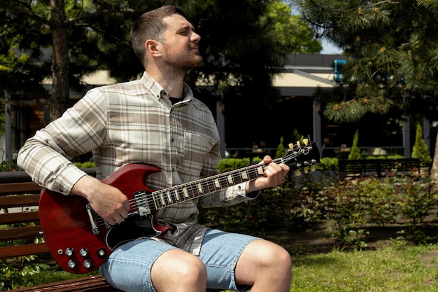 Un joven atractivo tocando la guitarra mientras está sentado en un banco