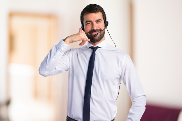 Joven con un auricular haciendo gesto de teléfono sobre fondo desenfocado