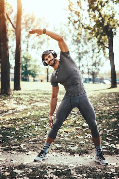 Joven con auriculares está haciendo ejercicio de estiramiento en la naturaleza otoñal y escuchando música.