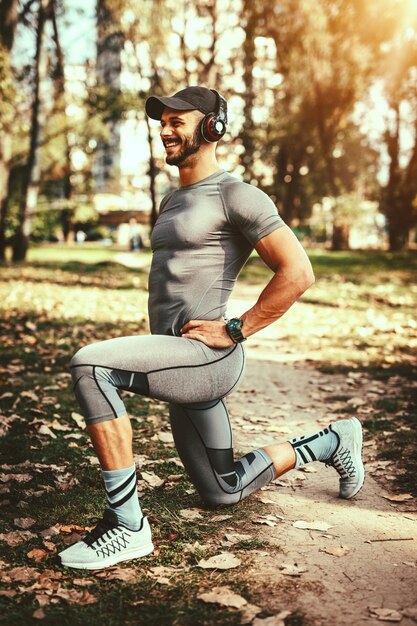 Joven con auriculares está haciendo ejercicio de estiramiento en la naturaleza otoñal y escuchando música.