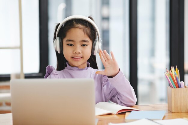 Una joven con auriculares está saludando a la cámara mientras está sentada en un escritorio