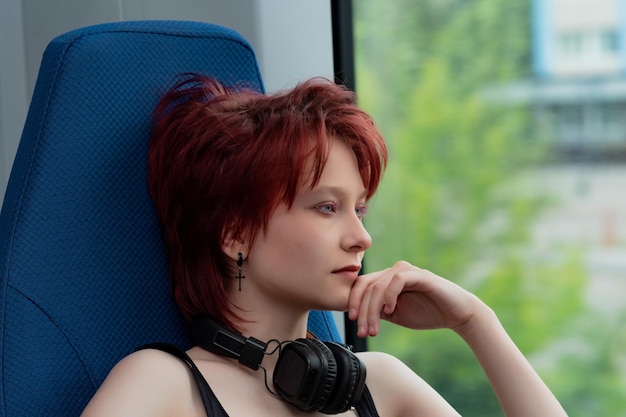 Una joven con auriculares viaja en un tren suburbano en movimiento y mira por la ventana