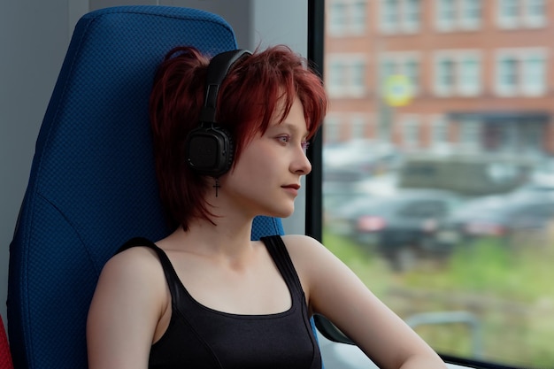 Una joven con auriculares viaja en un tren suburbano en movimiento y mira por la ventana