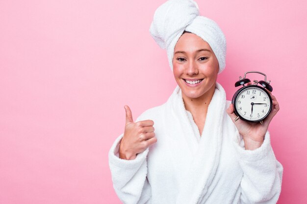 Joven australiana saliendo tarde de la ducha aislado sobre fondo rosa sonriendo y levantando el pulgar hacia arriba