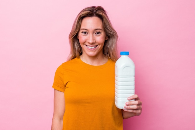 Joven australiana sosteniendo una botella de leche aislada sobre fondo rosa feliz, sonriente y alegre.