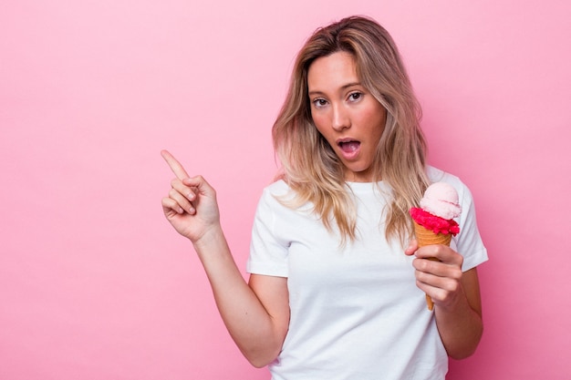 Joven australiana sosteniendo un helado aislado sobre fondo rosa apuntando hacia el lado